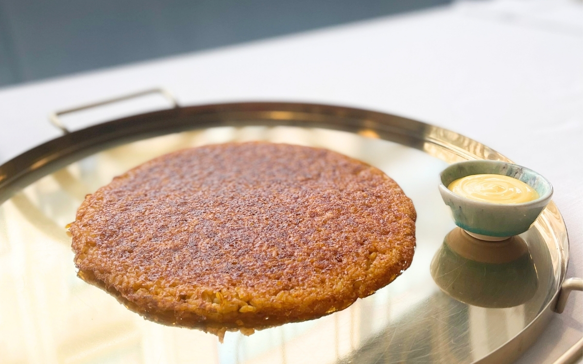 El Socarrat de Llisa Negra es una delicada capa de arroz caramelizado y crujiente, lleno de sabor a mar y técnica cuidada. Se sirve en pieza única, acompañado de alioli, como homenaje al arroz, solo los miércoles en el restaurante de Quique Dacosta en València.